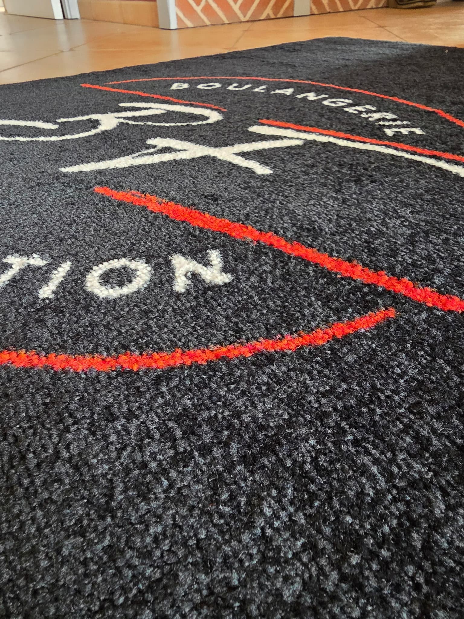 Photo réelle : détail du logo blanc et rouge sur le tapis Colorstar de la Boulangerie BF