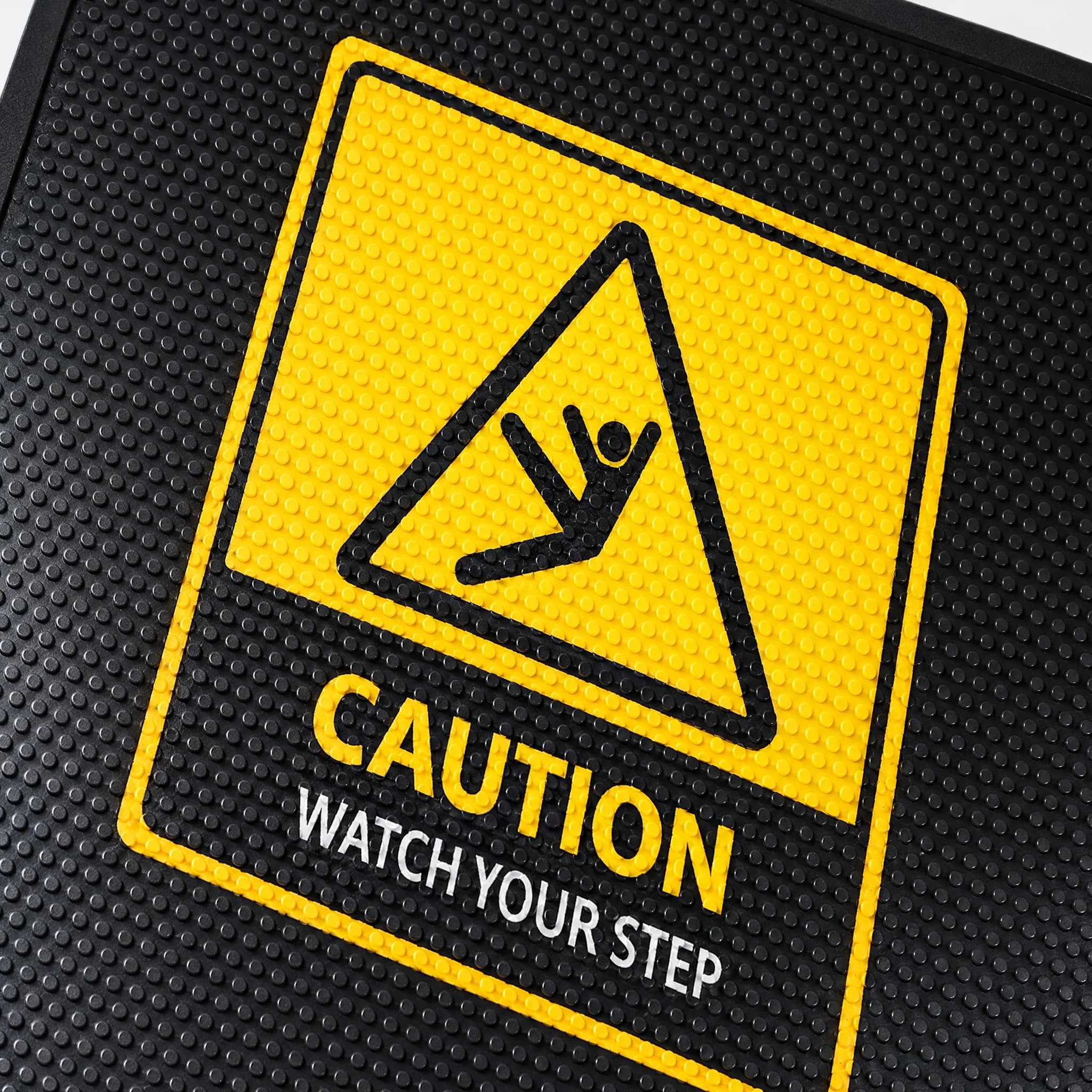 Illustration du SuperScrape Impressions en gros plan : reliefs ronds du caoutchouc noir et marquage jaune CAUTION, WATCH YOUR STEP