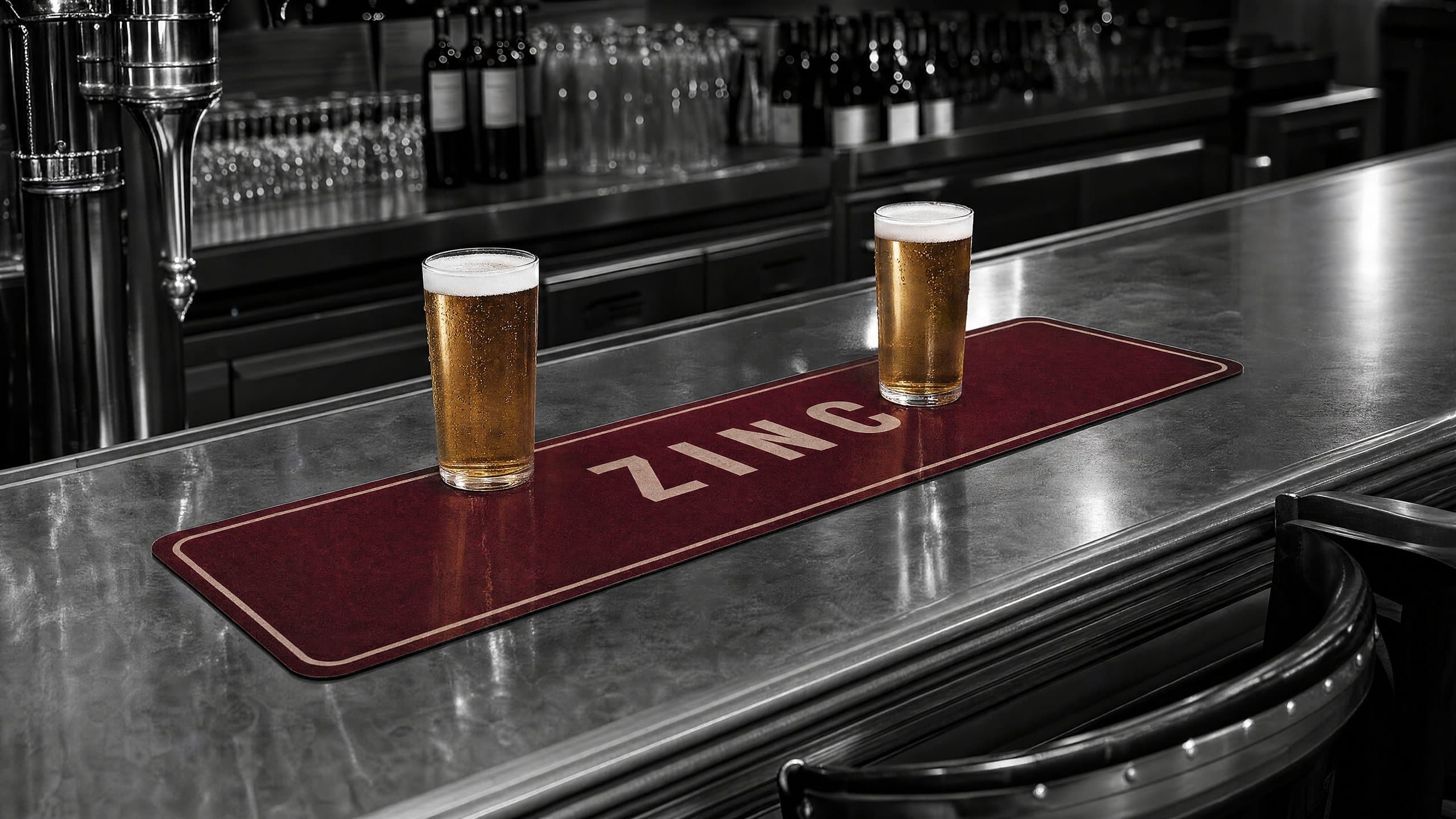 Tapis de bar bordeaux imprimé ZINC sous deux pintes de bière, sur un comptoir en zinc