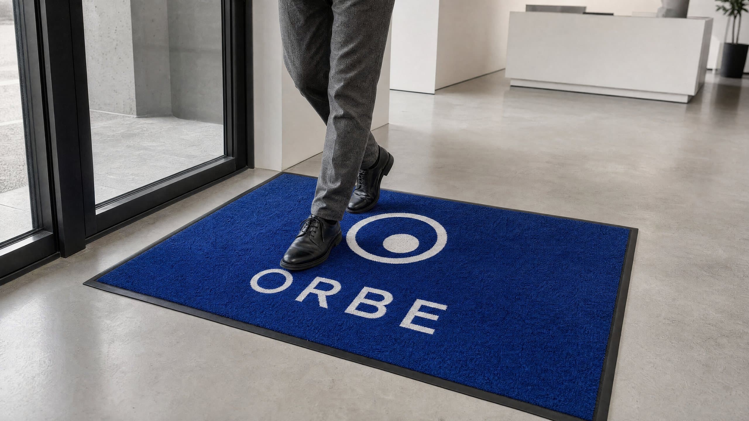 Tapis Colorstar bleu cobalt au logo blanc, posé dans le hall d’entrée de bureaux, une personne marche dessus