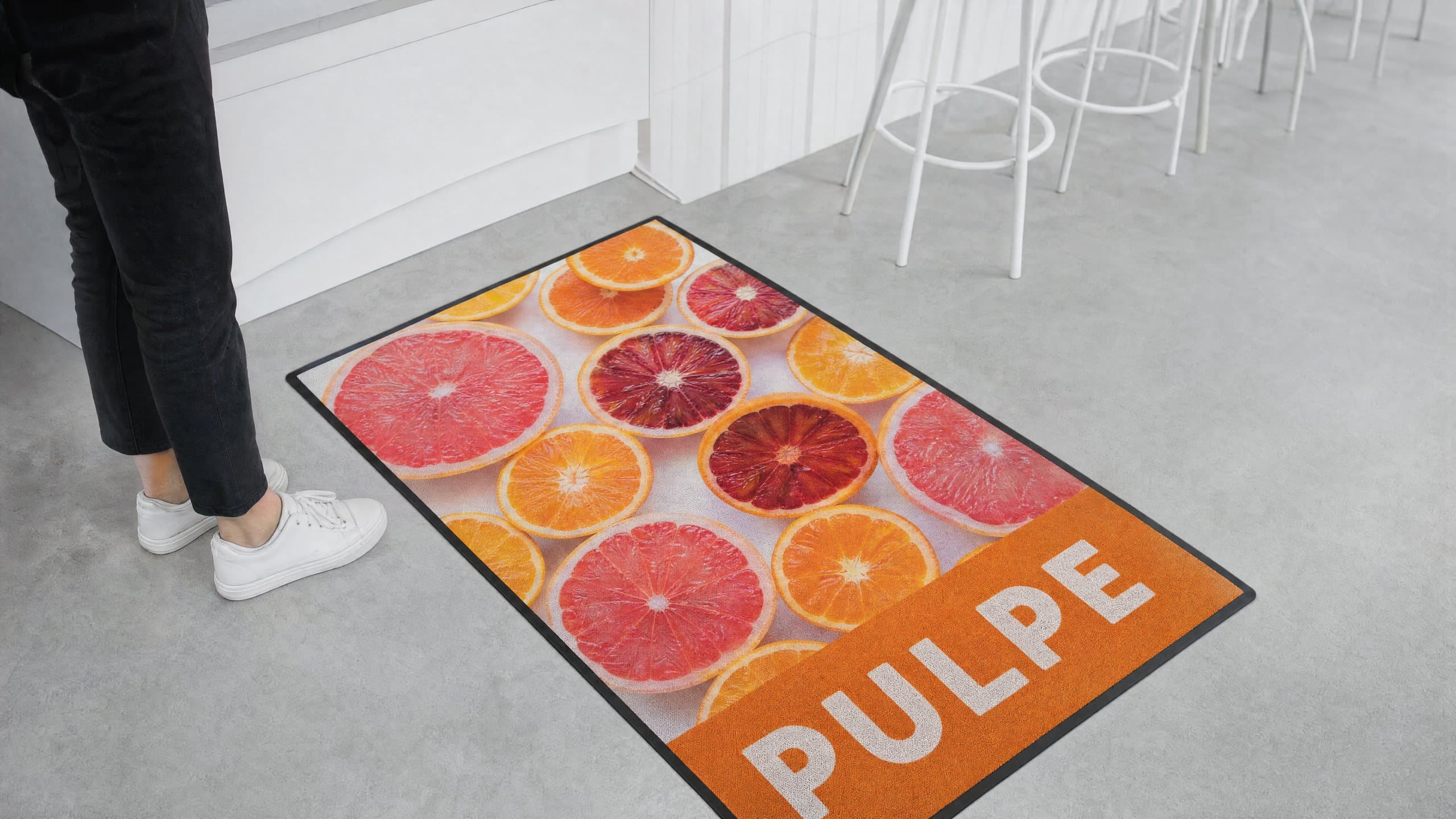 Tapis promotionnel imprimé d’une photo d’agrumes en tranches, posé au sol d’un bar à jus