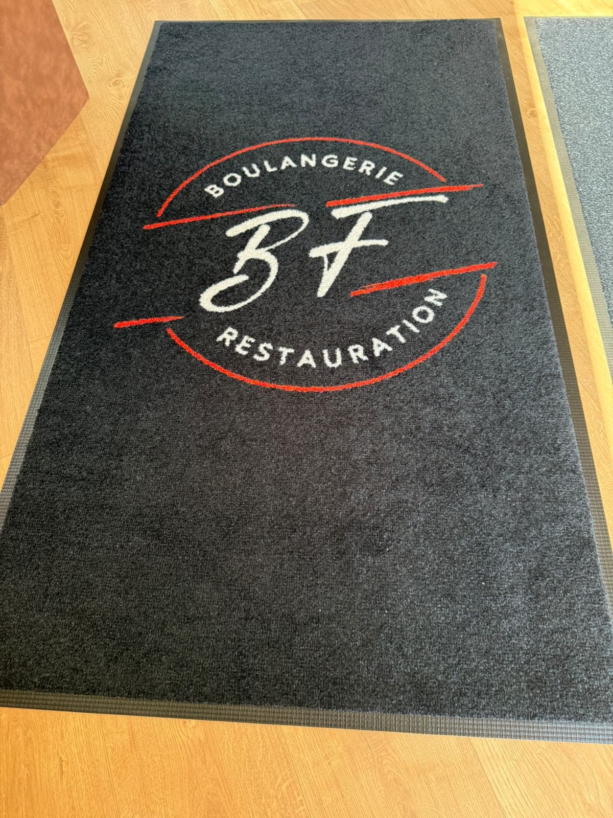 Tapis anthracite au logo BF vu en biais, de la tête au pied, avec sa bordure