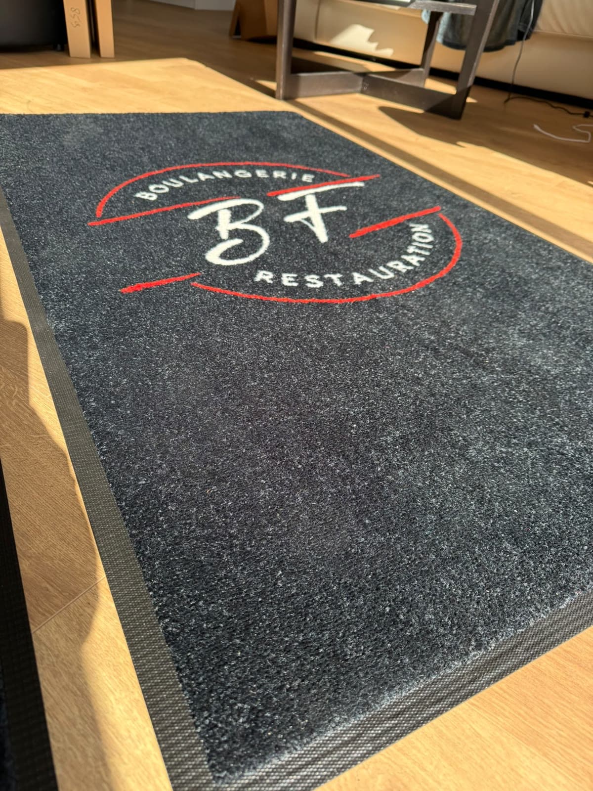 Tapis anthracite en lumière rasante : le logo, la surface et la bordure