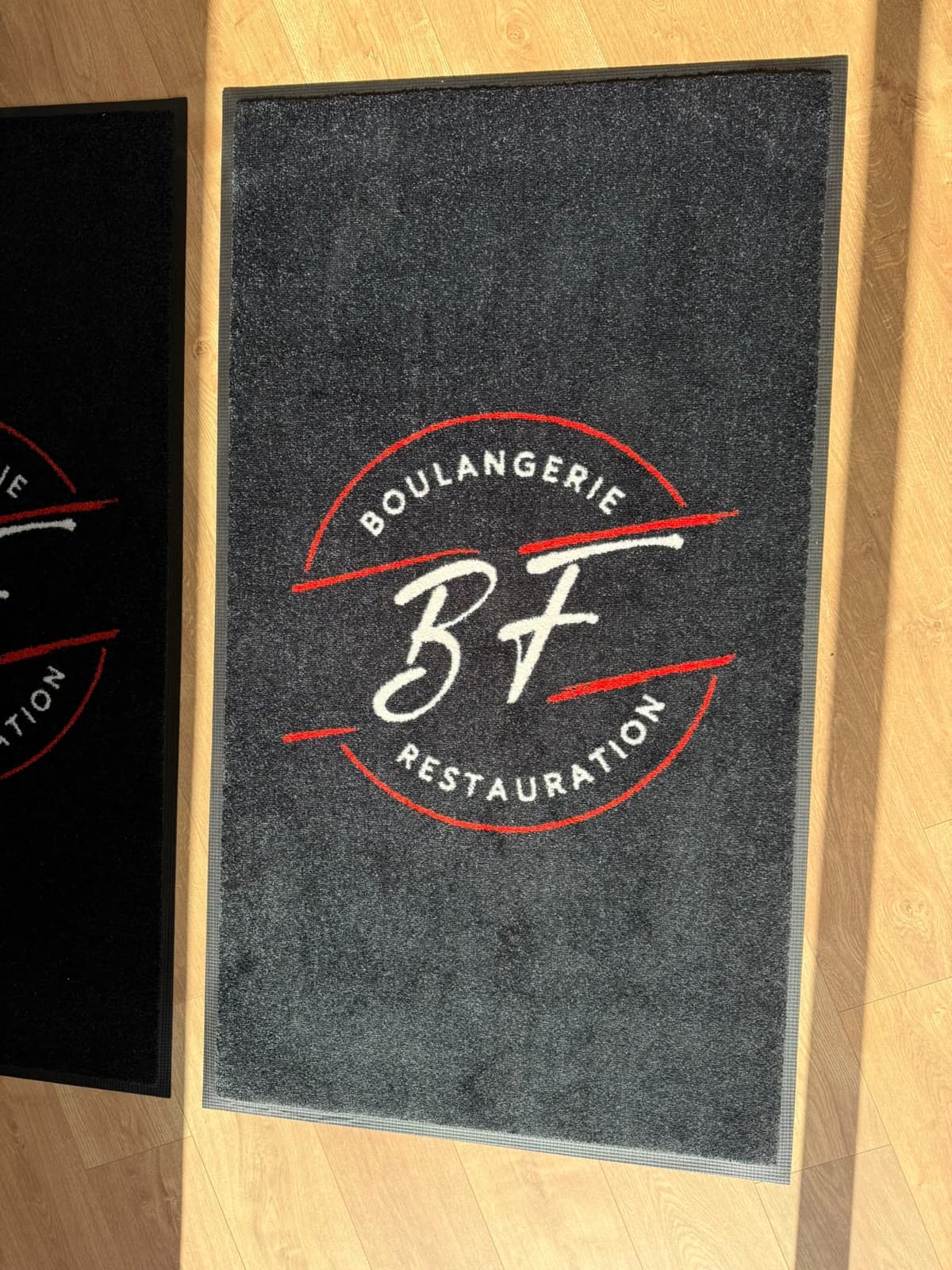 Tapis anthracite au logo blanc et rouge BF Boulangerie Restauration, vu de face