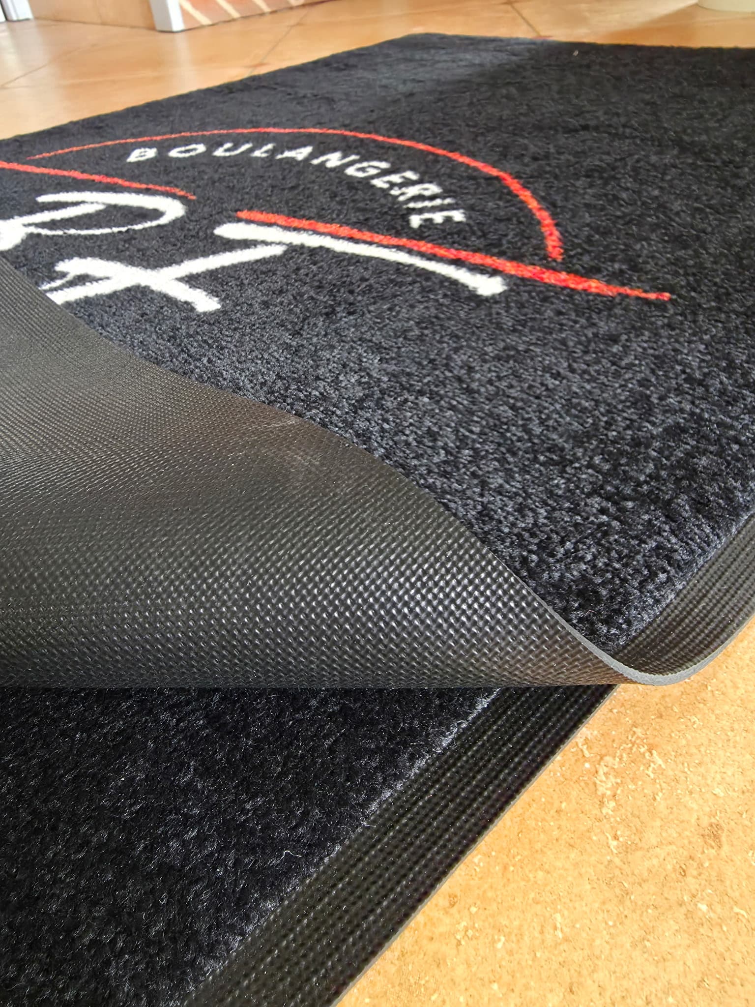 Coin du tapis Colorstar de la Boulangerie BF soulevé pour montrer son dessous