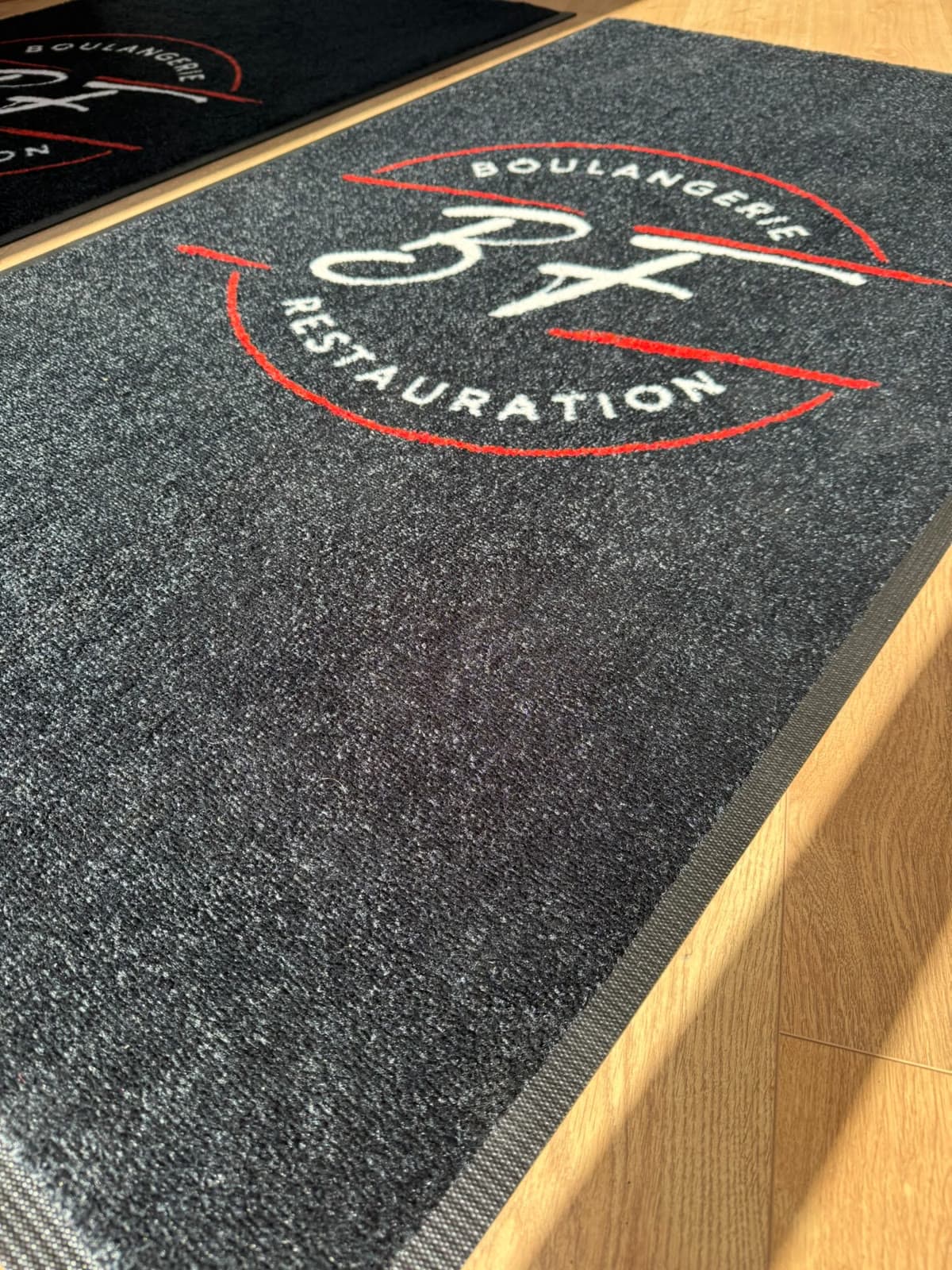 Gros plan sur le logo BF Boulangerie Restauration et la texture du tapis anthracite