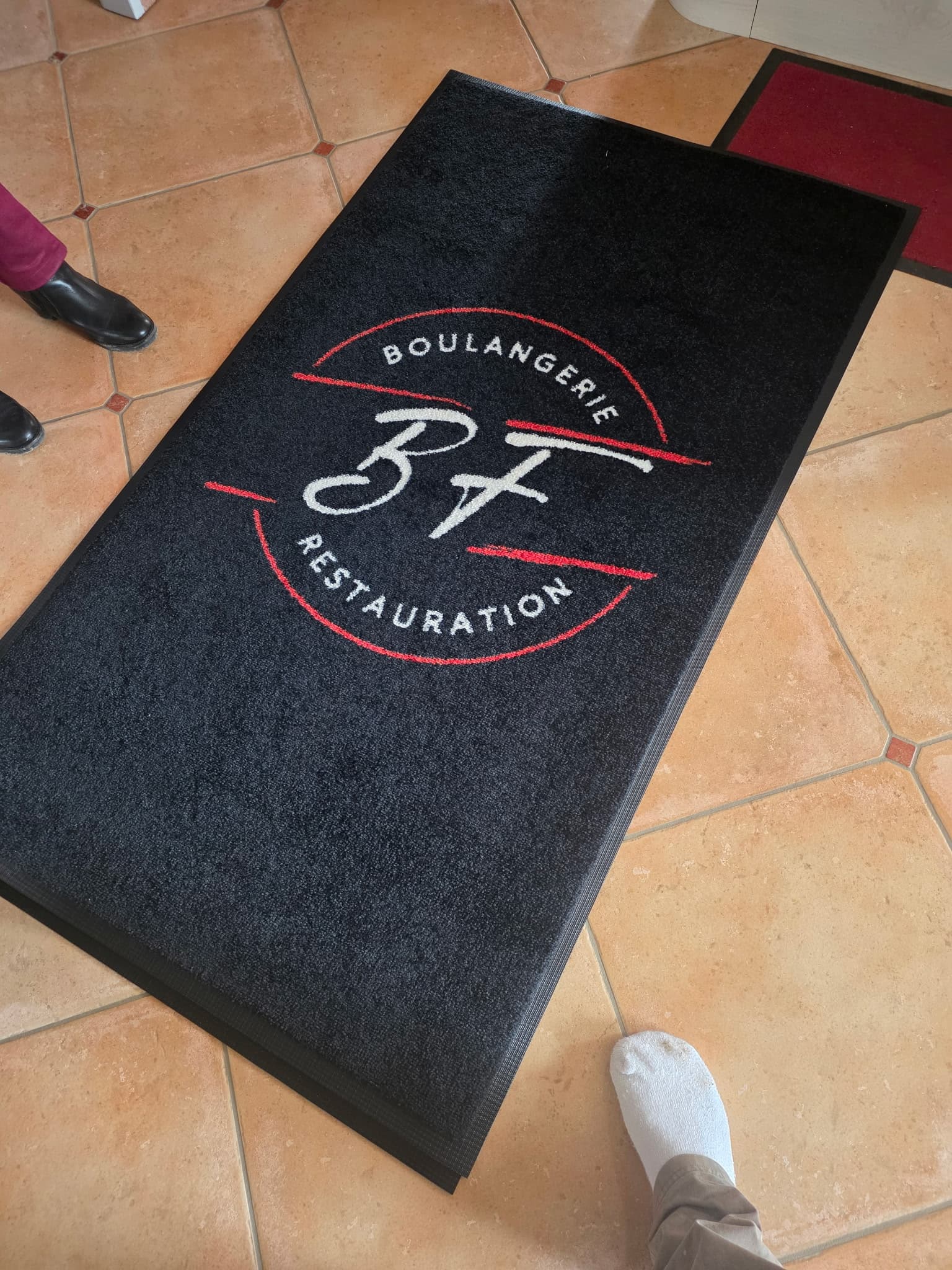 Réalisation Stride Rug : tapis noir avec le logo blanc et rouge BF Boulangerie Restauration, posé sur du carrelage