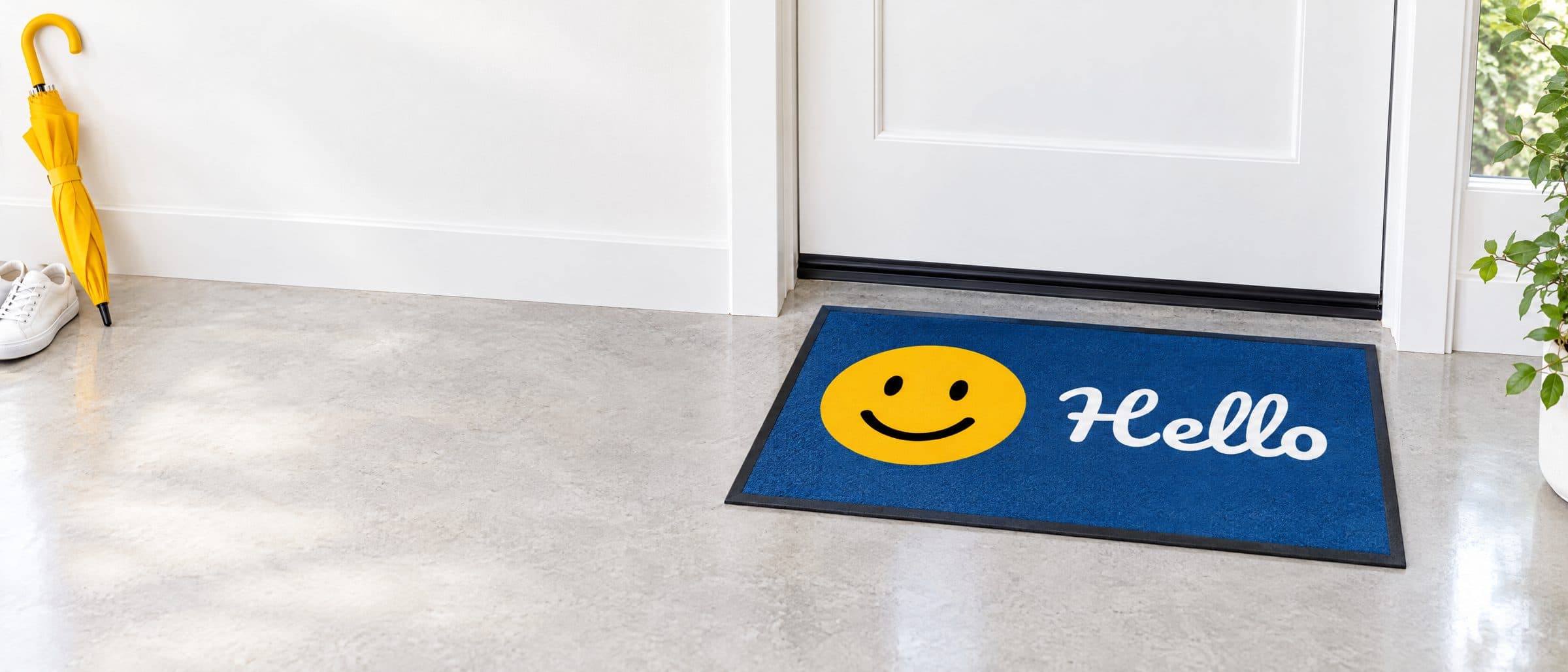 Tapis bleu avec un smiley jaune et « Hello » devant une porte d’entrée blanche